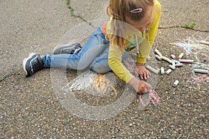 Child paints outdoors. Little girl drawing colored chalk on the asphalt . Creative development of children