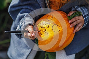 A child paints a scary Halloween face on a pumpkin. Children are preparing for the feast of all saints. Children& x27;s