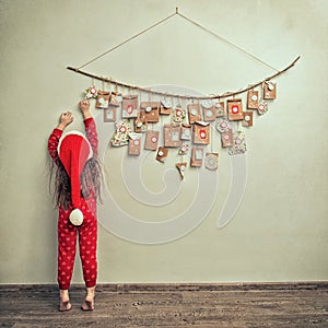 Child in pajamas and Christmas cap stretches for advent calendar with small gifts. kid counts days until new year
