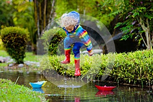 Child with paper boat in puddle. Kids by rain