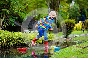 Child with paper boat in puddle. Kids by rain