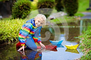 Child with paper boat in puddle. Kids by rain