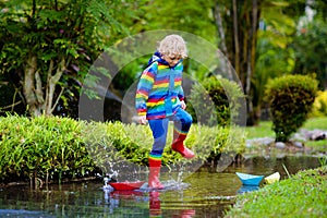 Child with paper boat in puddle. Kids by rain