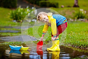 Child with paper boat in puddle. Kids by rain.