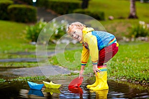 Child with paper boat in puddle. Kids by rain