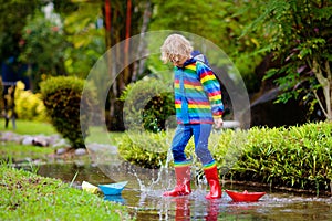 Child with paper boat in puddle. Kids by rain