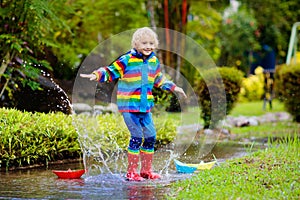 Child with paper boat in puddle. Kids by rain