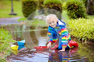 Child with paper boat in puddle. Kids by rain