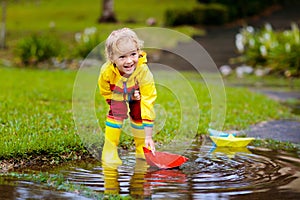 Child with paper boat in puddle. Kids by rain