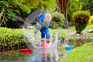 Child with paper boat in puddle. Kids by rain