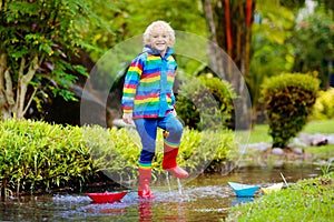 Child with paper boat in puddle. Kids by rain