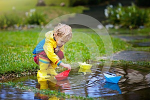 Child with paper boat in puddle. Kids by rain