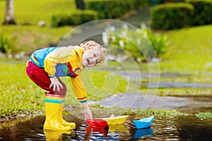 Child with paper boat in puddle. Kids by rain