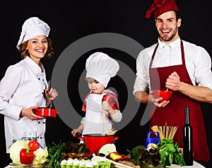 Child with parents cooking at kitchen. Happy family preparing breakfast or dinner together. Homemade food. Parents