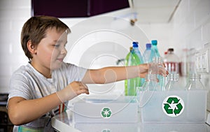 A child participates in sorting plastic in the kitchen to be sent for recycling. Cute boy child putting a plastic bottle