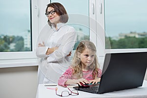 A child patient in the doctor office is sitting at the table, looking at the laptop.