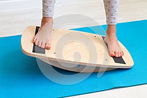The child performs exercises on thewooden balancer from the valgus of the foot. The child& x27;s legs are close-up. Physical