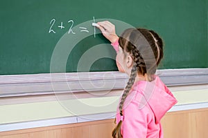 The child performs a learning task. Babe starts school in first grade.Little girl draws with chalk on a blackboard. School concept