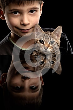 Child with a pet. A boy with a kitten on a black background is reflected in the mirror