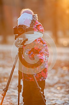 Child photographer taking pictures on camera using tripod, sunset light