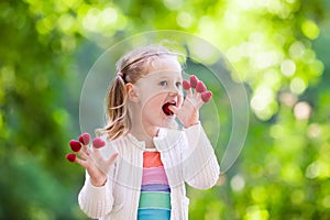 Child picking and eating raspberry in summer