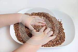 A child picks up buckwheat porridge, hands of a child and porridge on a white background photo