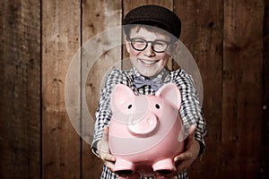 Child, piggy bank or excited in portrait by studio background, savings or finance lesson in youth. Boy, smile and face