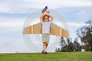 Child pilot aviator with with paper wings or toy airplane dreams of traveling in summer in nature.