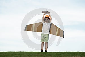 Child pilot aviator with with paper wings or toy airplane dreams of traveling in summer in nature.