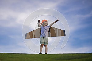 Child pilot aviator with with paper wings or toy airplane dreams of traveling in summer in nature.