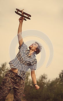 Child pilot aviator with plane at sunset, little boy playing with cardboard toy airplane outdoors, against summer sky background.