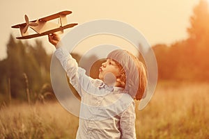 Child pilot aviator with plane at sunset, little boy playing with cardboard toy airplane outdoors, against summer sky background.