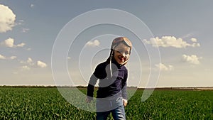 A child in a pilot`s suit runs along the green field, showing his hands the flight of the aircraft at a slow pace