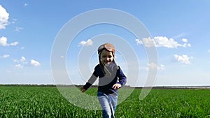 The child in the pilot`s suit runs along the green field, showing his hands the flight of the plane, in slow motion