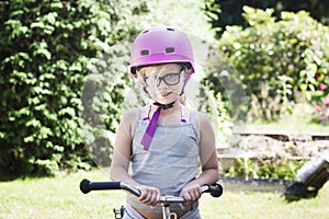 Child with pink bicycle helmet and black glasses on bike