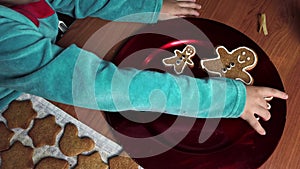 Child placing gingerbread man cookie on a red plate with other cookies. Gingerbread man family