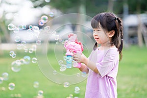 Child play with the bubble gun and have fun. Happy children standing in the grass. Sweet smile of a little girl. Time to relax.