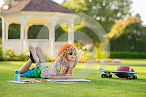 Child play and draw craft artwork homework. Clever school boy doing homework, writing on copy book in green grass of