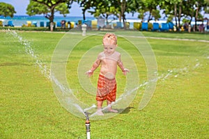 Child play, swim and splash under water sprinkler spray