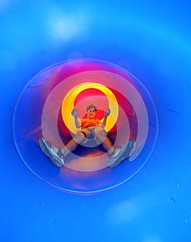 Child on the playground comes down in a big blue tunnel slide