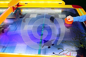 Child is playing air hockey game and holding striker. Mallets and puck in hands. Violet table with pattern. Game in entertainment