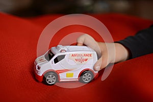 Child playing with ambulance car toy on a red carpert