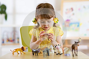 Child playing with animal toys at table in kindergarten or home