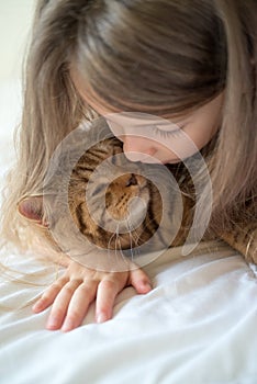 Child playing with cat on bed