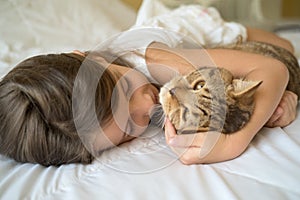 Child playing with cat on bed