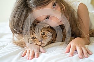 Child playing with cat on bed