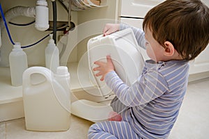 A child is playing with chemical cleaning products under the sink in the