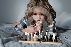 Child playing chess on bed. Child think about chess game. Intelligent, smart and clever school kid pupil. Games for