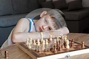 The serious child lost in thought playing chess. Playing board games, on coronavirus quarantine. The child playing chess