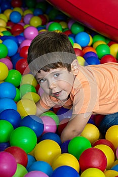 Child playing with colorful balls in playground ball pool. Activity toys for little kid. Kids happiness emotion having fun in ball